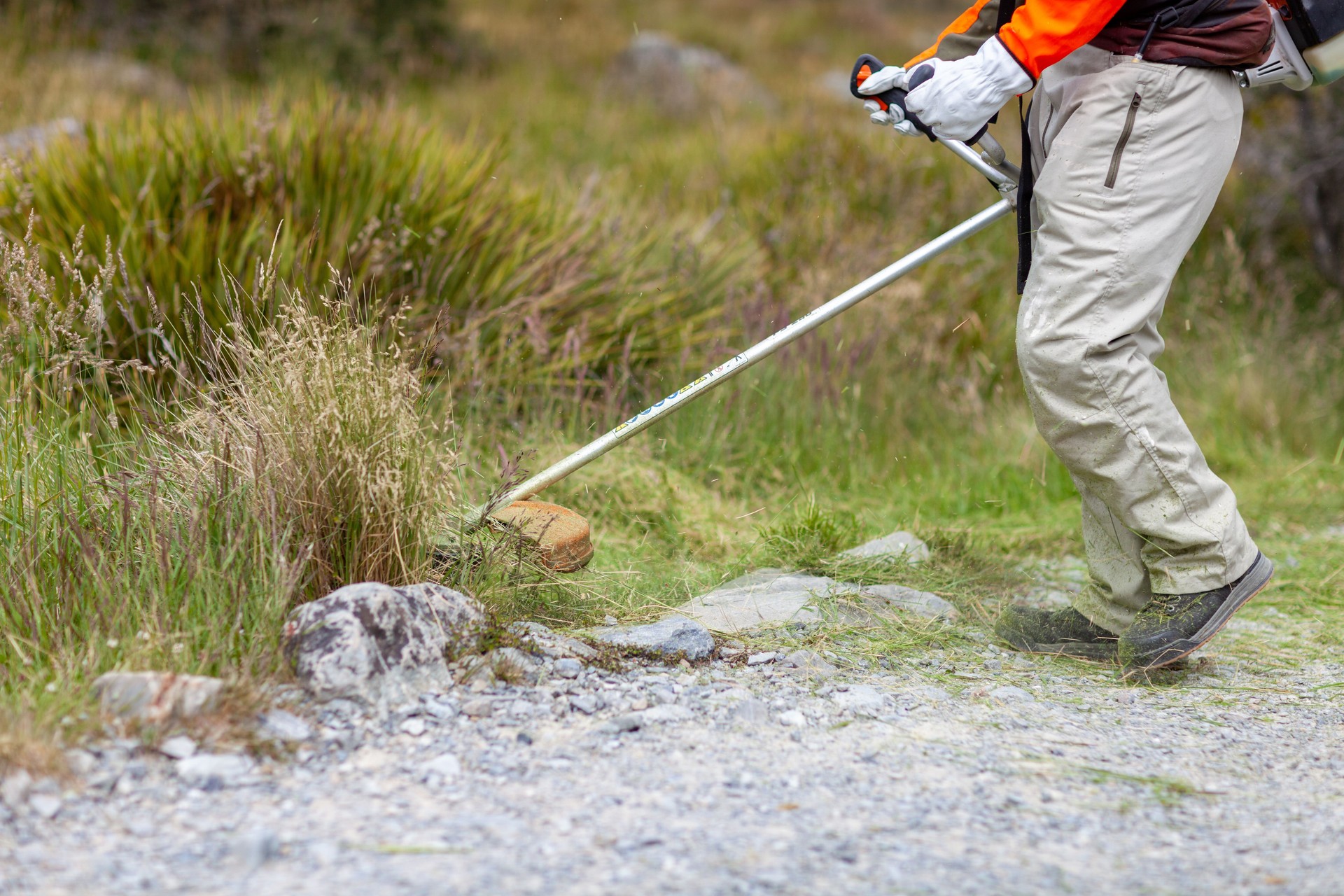 Young worker mowing lawn with grass trimmer outdoors in garden. Professional roadside mowing lawn.  Photo of maintenance professional worker cutting ground grass.